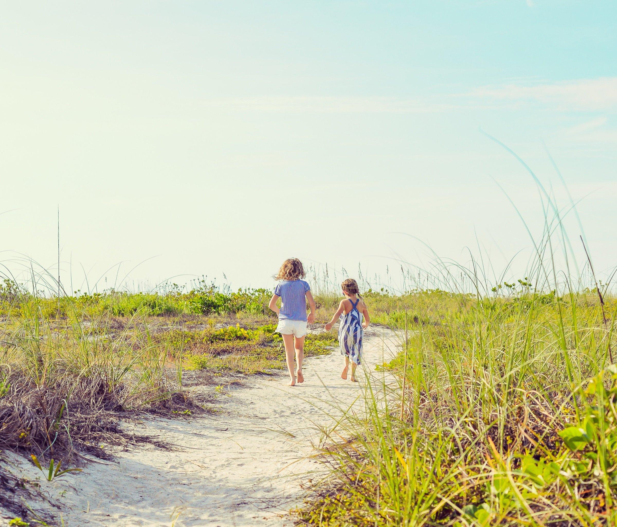 Children running on a sandy path through dunes towards the beach